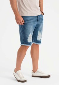 Jeansshorts i ljusblått med slitna detaljer och fransad fåll. Återfinns med vita sneakers med bruna accenter.