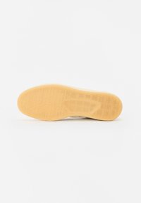 Talpa de sneaker din cauciuc de culoare bej, cu un model texturat de fagure. Marginile curbate îmbunătățesc aderența și flexibilitatea, având o finisare exterioară netedă.