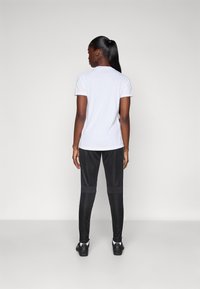 White short-sleeve t-shirt and black pants with gray accents, featuring a fitted design, visible stitching, and athletic footwear.