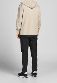 Felpa beige con una vestibilità comoda, abbinata a pantaloni cargo neri con tasche laterali. Sneakers nere con dettagli bianchi completano l'outfit.