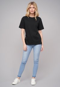 Černé bavlněné tričko s krátkými rukávy a kulatým výstřihem, spárované se světle modrými skinny džíny a bílými teniskami, umístěné na neutrálním pozadí.