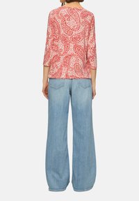 Rode blouse met paisleypatroon en driekwartmouwen, gecombineerd met lichtblauwe wijde jeans. De stof lijkt lichtgewicht met een zachte textuur.