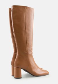O pereche de cizme din piele bej, până la jumătatea gambei, cu vârful rotund, tocuri bloc și un finisaj neted, prezentate pe un fundal alb.