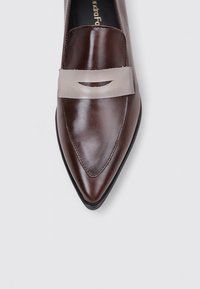 Zapato de cuero marrón con punta afilada y una tira gris claro a lo largo del empeine. Superficie lisa con un brillo sutil y bordes limpios.