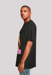 Black cotton t-shirt featuring a front graphic of a person with long hair, text "Money" in pink at the bottom. Loose fit, short sleeves.