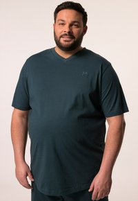 Camiseta de manga corta en verde oscuro, con escote en V, hecha de tela suave, que presenta un sutil logotipo en el pecho, ofreciendo un ajuste relajado y una textura lisa.