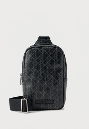 Črna sintetika torbica čez ramo z vzorcem diamantov, zadrgo in nastavljivim trakom. Spredaj okrasni logotip. Gladek otip.