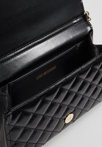 Borsa nera trapuntata in pelle sintetica con chiusura a scatto color oro. Interno con scomparto per carte con "LOVE MOSCHINO" impresso in oro.