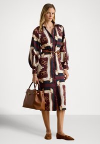 Rochie lungă cu model în vișiniu, crem și bleumarin, cu curea și mâneci supradimensionate. Geantă de mână maro din piele și mocasini asortați.