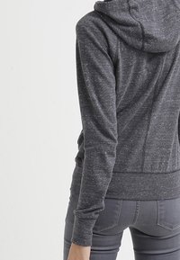 Grå, lätt hoodie med en texturerad tyg, en rymlig huva och åtsittande ärmslut. Har en slank, modern design med minimala sömmar.