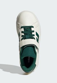 White sneaker with dark green laces, stripes, and padded tongue, featuring a Velcro strap and Adidas branding inside.