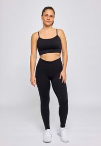 Top court noir côtelé avec des bretelles fines associé à des leggings noirs taille haute, tous deux avec une coupe ajustée, présentés sur un fond uni.