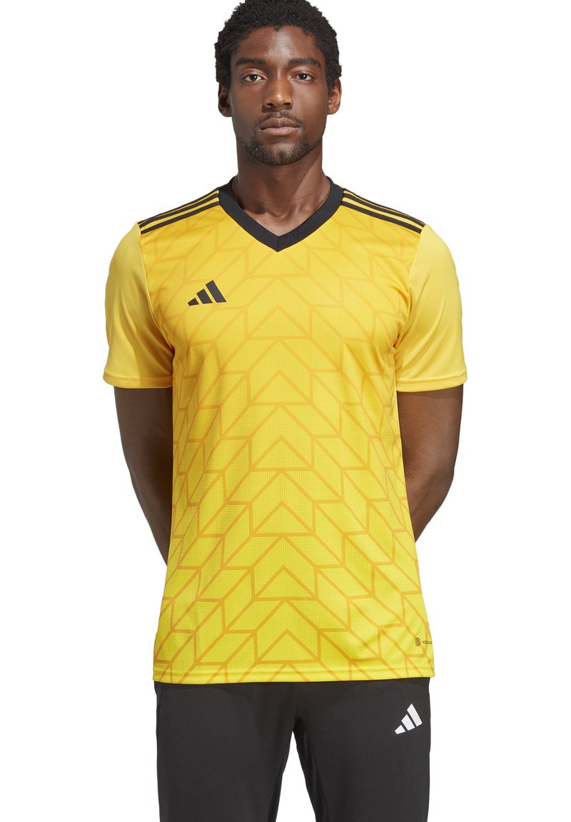 Maglia sportiva gialla con motivo geometrico, design a V e accenti neri sulle spalle. Realizzata in tessuto leggero.