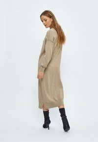 Bež haljina od pletenine s dugim rukavima, do gležnjeva i sa bočnim prorezima. Model je kombinirao s crnim čizmama s visokom potpeticom. Glatka tekstura.