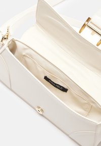 Sac besace beige ouvert montrant la doublure intérieure en tissu, une petite poche intérieure, et une fermeture à rabat aimantée et boucle en métal doré.