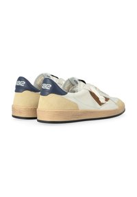 Sneakers bianchi e beige realizzati in materiali scamosciati e in pelle, con accenti tonali, suole beige testurizzate e un tallone blu navy con branding.