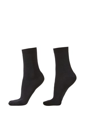 Paire de chaussettes noires unies mi-mollet présentée sur des modèles de pieds inclinés sur fond blanc.