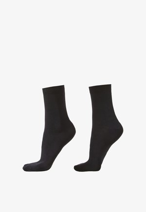 Paire de chaussettes noires unies mi-mollet présentée sur des modèles de pieds inclinés sur fond blanc.