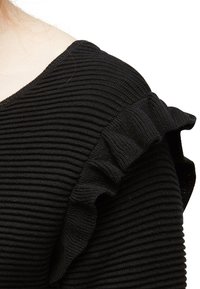 Svart ribbad topp med texturerad tyg, en v-ringning och volangdetaljer vid axlarna, vilket skapar ett lagerpåverkan.