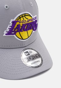 Gray adjustable cap featuring a Los Angeles Lakers embroidered logo in purple and yellow on the front, with a round logo sticker on the brim.