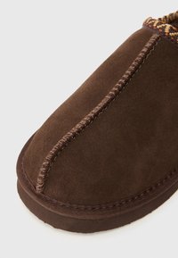 Brune suede hjemmesko med rund tå, kontrasterende syede syninger og tekstureret trim langs kraven. Blød indvendig foring synlig.