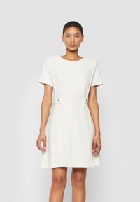 Witte jurk met korte mouwen en een ronde halslijn, een uitlopende rok en zijknopen. Gemaakt van soepele stof met een schone, minimalistische uitstraling.