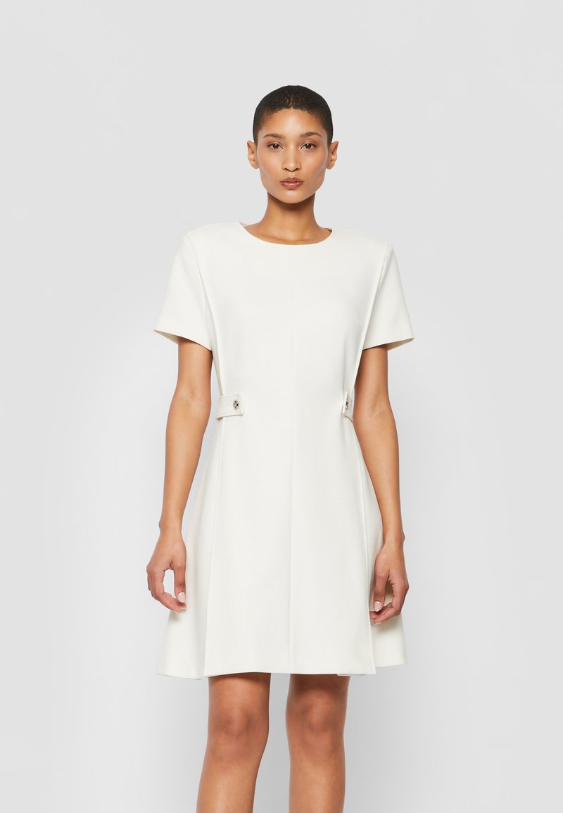 Witte jurk met korte mouwen en een ronde halslijn, een uitlopende rok en zijknopen. Gemaakt van soepele stof met een schone, minimalistische uitstraling.