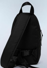 Sac à dos en tissu noir avec une forme épurée, une bandoulière réglable et une poche zippée sur le côté pour le rangement. Matériau texturé et durable.