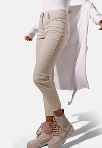 Beige ribbel skinny broek met een slim fit, gecombineerd met lichtbeige enkelboots met veters en een rits. Witte lange mouwen top valt iets losjes.