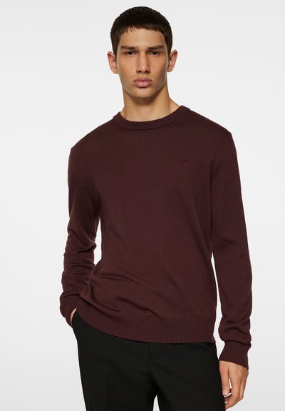 Bordeaux gebreide sweater met ronde halslijn en lange mouwen. Gladde textuur, geribbelde boorden en onderkant, met een subtiel logo detail op de borst.