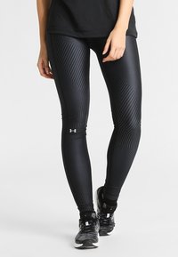 Czarne legginsy sportowe z fakturowanym wzorem, dopasowanym krojem i odblaskowymi akcentami, w połączeniu z czarnymi butami sportowymi i czarnym t-shirtem.