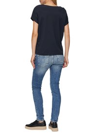 Marineblauwe katoenen t-shirt met korte, opgerolde mouwen, gepaard met lichtblauwe denim jeans. Zwarte sneakers met een gestructureerde zool.
