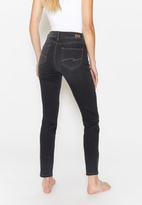 Jeans skinny in denim nero con vita alta, dotati di tasche posteriori e cuciture a contrasto. Texture liscia, design aderente e dettagli minimi.