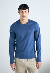 T-shirt en coton bleu à manches longues avec un col rond et un petit logo blanc "BOSS" sur la poitrine. Texture lisse et design ajusté.