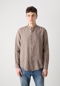 Lichtbruine linnen blouse met een mandarinakraag, lange mouwen en knopen aan de voorkant. G gedragen met blauwe denim jeans.