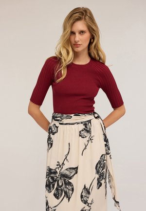 Haut côtelé bourgogne à manches courtes associé à une jupe crème avec des motifs floraux noirs et une taille nouée. Tissu doux avec un design ajusté.