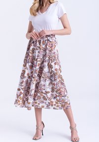 Haut blanc à manches courtes avec encolure à volants, associé à une jupe longue à motifs avec des dessins cachemire dans des tons rose, orange et marron.