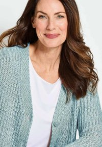 Helles blaues Strickjacke mit einem strukturierten Muster, mit V-Ausschnitt und zwei vorderen Knöpfen. Getragen über einem weißen Hemd.