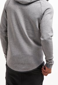 Grå hoodie med en mjuk textur, med rund nederkant, sidofickor och löstagbar huva. Manschetterna och nederkanten är åtsittande för en snug passform.