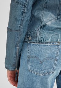 Giubbotto di pelle blu con finitura testurizzata, maniche con zip e minuteria in metallo. Abbinato a jeans di denim blu chiaro con design delle tasche posteriori.