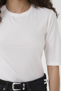 White short-sleeve shirt worn with black belt and black pants, showing mid-torso and arm of person with curly hair.