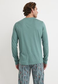 Langarm turquoise shirt met een rechte zoom, gecombineerd met gestreepte pyjamabroek met nutcracker ontwerpen op een grijze achtergrond.