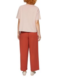 Kortärmad lichtroze top gecombineerd met losse, wijde roestkleurige broek. Getextureerde stof, relaxte pasvorm en minimalistisch ontwerp.
