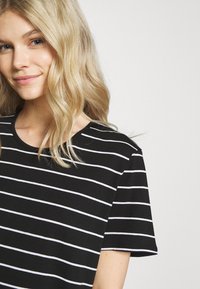 T-shirt nera a maniche corte con strisce orizzontali bianche, con colletto rotondo e una texture di stoffa morbida.