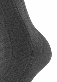 Chaussette gris foncé avec un motif texturé et des côtes subtiles. Façonnée pour épouser le pied, mettant en valeur des coutures renforcées au niveau du talon.