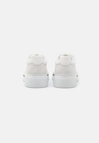 Baskets blanches avec une tige en cuir lisse et des accents en daim texturé. Œillets arrondis et logo sur le talon. Semelle en caoutchouc épaisse.