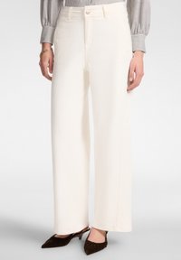 Pantaloni bianchi a gamba larga realizzati in tessuto texturizzato con vita alta e chiusura con bottone frontale, abbinati a tacchi a punta marrone scuro.