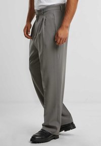 Pantalones grises con pliegues, hechos de una tela suave, con una cinturilla ajustada y piernas acampanadas, combinados con zapatos negros.