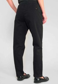 Zwarte katoenen broek met een rechte snit, voorzien van een achterzak en subtiele logomarkering. Gecombineerd met stijlvolle zwarte schoenen.