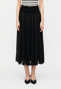 Μακριά μαύρη φούστα από ελαφρύ υλικό με φαρδιά μέση. Διαθέτει απαλές πιέτες, που τελειώνουν λίγο πάνω από τους αστραγάλους. Φοριέται με μαύρα παπούτσια.